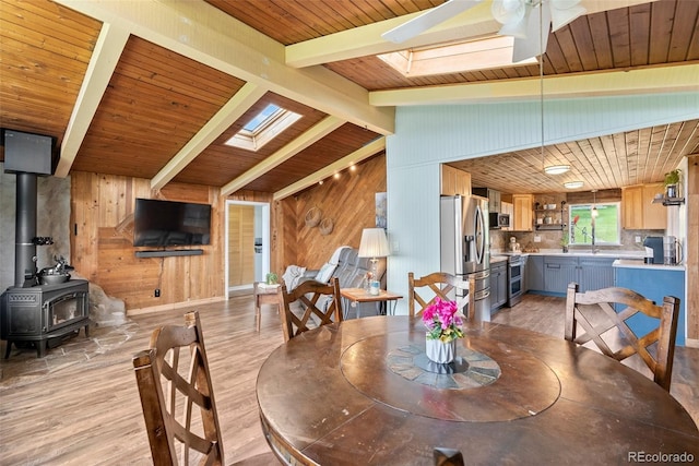 dining space featuring a wood stove, ceiling fan, vaulted ceiling with skylight, and light wood-type flooring