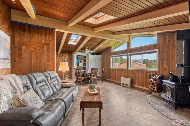 living room featuring wood walls, a wood stove, wooden ceiling, vaulted ceiling with skylight, and ceiling fan