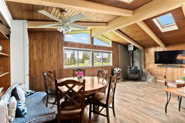 dining space with wood ceiling, lofted ceiling with skylight, ceiling fan, hardwood / wood-style flooring, and a wood stove