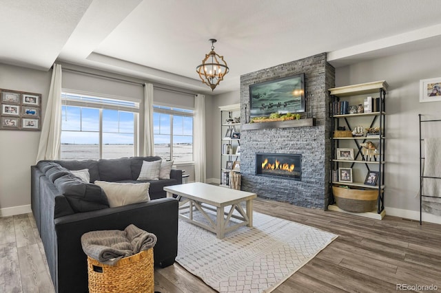 living area with a water view, a stone fireplace, baseboards, and wood finished floors