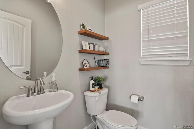 half bathroom with a sink, toilet, and baseboards