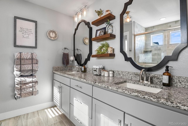 full bathroom with double vanity, a stall shower, baseboards, and a sink