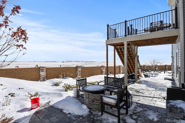 snow covered patio featuring stairs and a fenced backyard