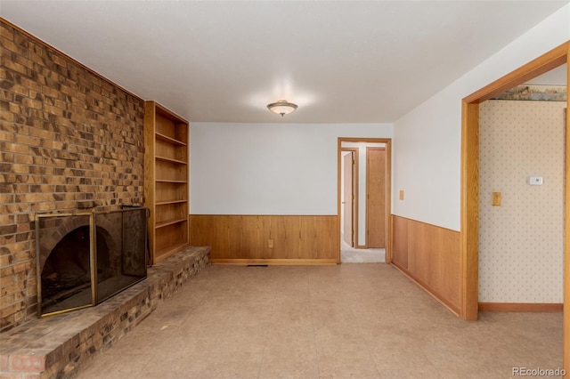 unfurnished living room with built in shelves, wooden walls, and a brick fireplace