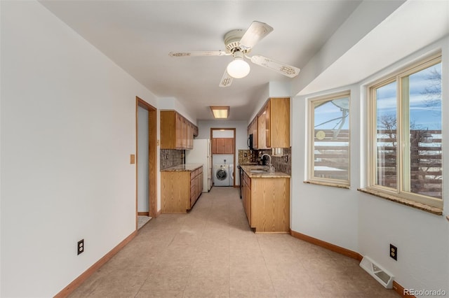 kitchen featuring washing machine and clothes dryer, ceiling fan, sink, white fridge, and decorative backsplash