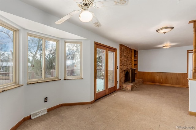 unfurnished living room with ceiling fan, wood walls, and a brick fireplace