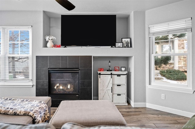 interior space with a tiled fireplace, wood finished floors, a ceiling fan, and baseboards