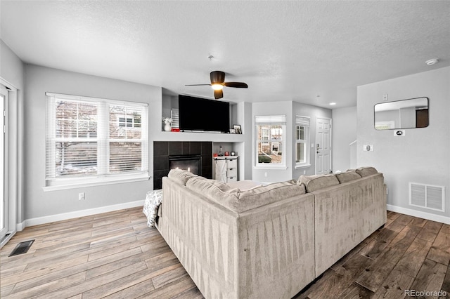 living room with wood finished floors, a tile fireplace, visible vents, and baseboards