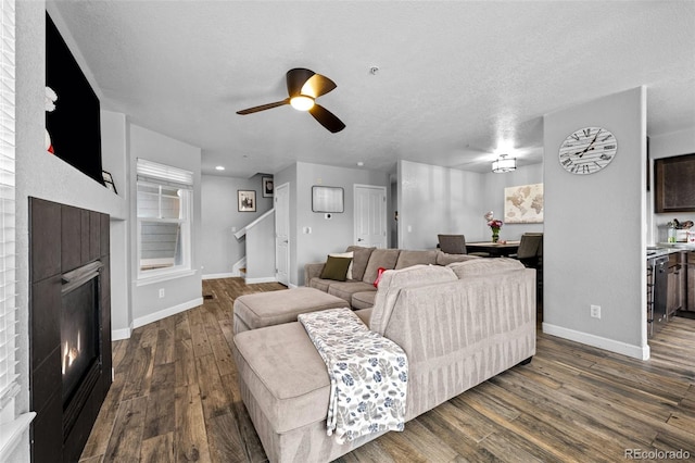 living area featuring dark wood finished floors, a textured ceiling, a warm lit fireplace, baseboards, and stairs