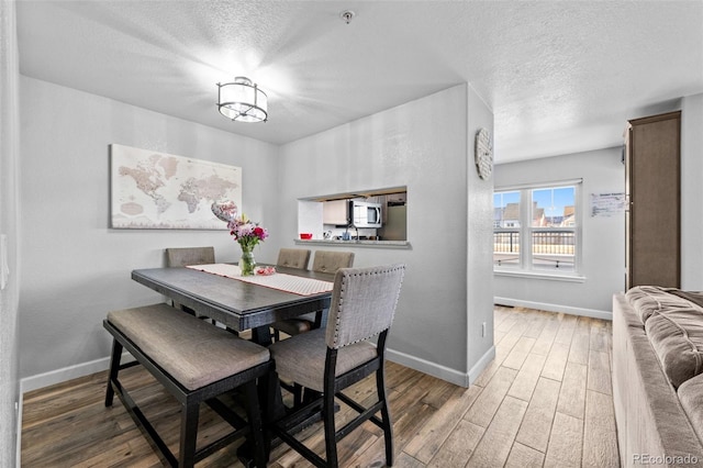 dining space featuring a textured ceiling, wood finished floors, and baseboards