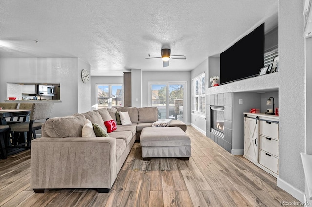 living area featuring light wood-style floors, a tile fireplace, a textured ceiling, and baseboards