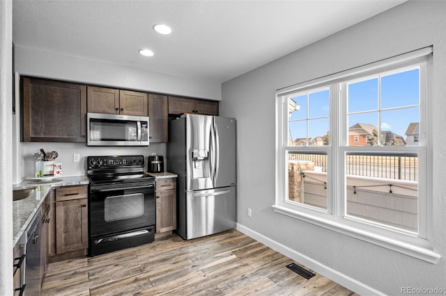 kitchen with stainless steel appliances, a wealth of natural light, visible vents, and light stone countertops