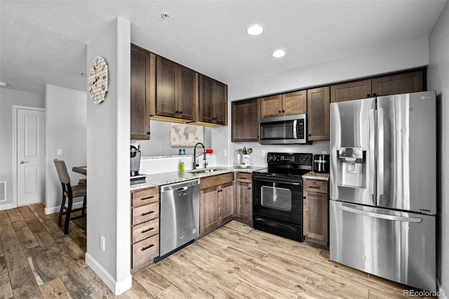 kitchen with light wood-style flooring, a textured ceiling, appliances with stainless steel finishes, and a sink