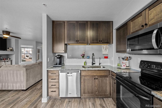 kitchen with stainless steel appliances, light wood-type flooring, a sink, and light stone countertops