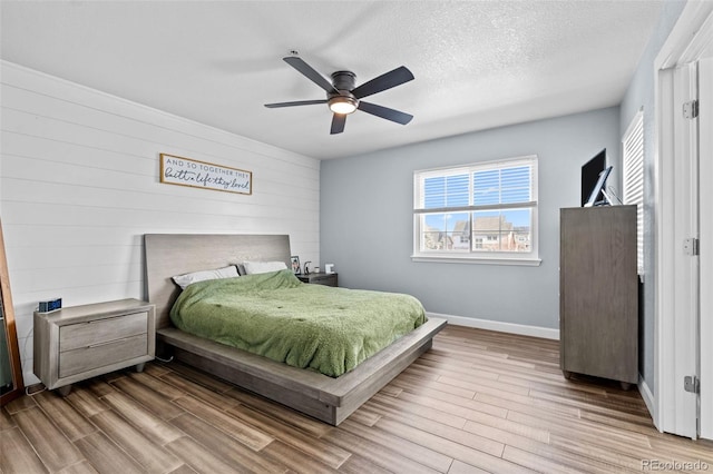 bedroom with light wood-type flooring, ceiling fan, baseboards, and a textured ceiling