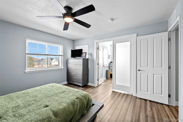 bedroom featuring a textured ceiling, wood finished floors, a ceiling fan, visible vents, and baseboards