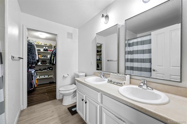 full bath featuring a sink, wood finished floors, a walk in closet, and visible vents