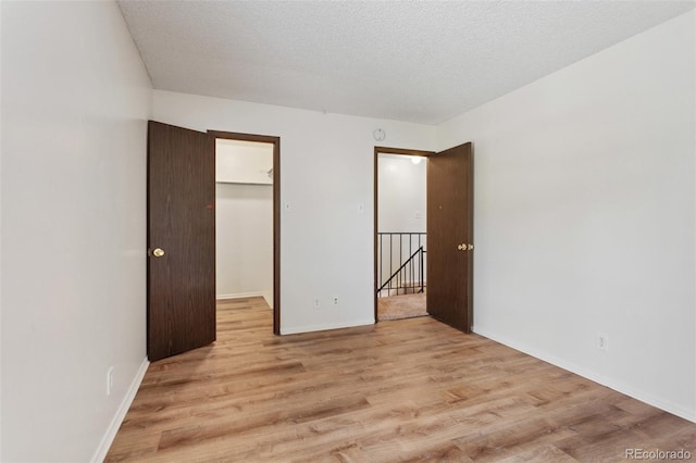 6650 E Arizona Ave Unit 203, Denver, CO 80224 - unfurnished bedroom featuring light wood finished floors, a walk in closet, baseboards, and a textured ceiling
