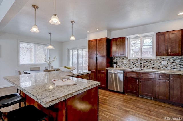 kitchen with a breakfast bar, sink, hanging light fixtures, a center island, and stainless steel dishwasher