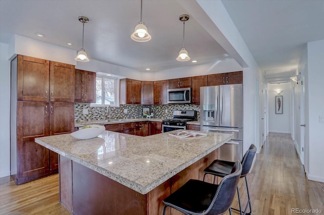 kitchen featuring pendant lighting, light hardwood / wood-style flooring, stainless steel appliances, a kitchen island, and decorative backsplash