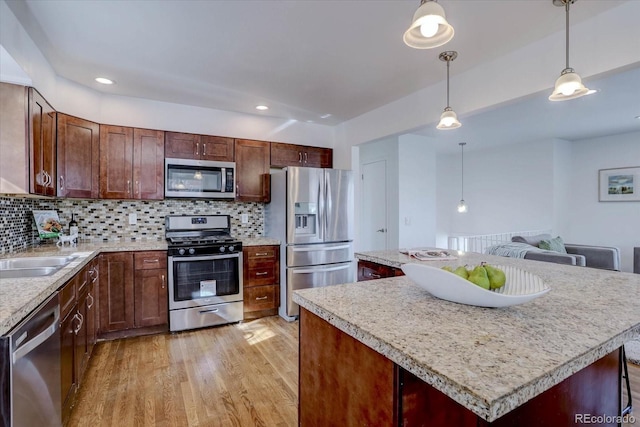 kitchen with pendant lighting, light hardwood / wood-style flooring, appliances with stainless steel finishes, a kitchen island, and decorative backsplash