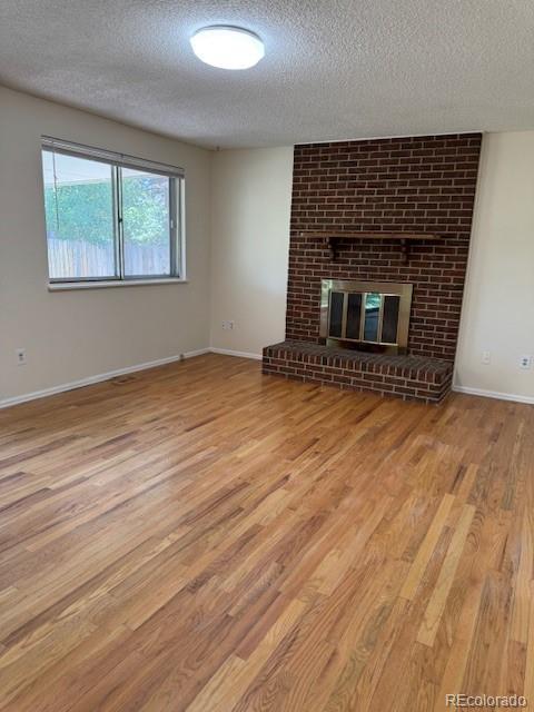 16180 E Flora Pl, Aurora, CO 80013 - unfurnished living room with a textured ceiling, wood finished floors, baseboards, and a brick fireplace