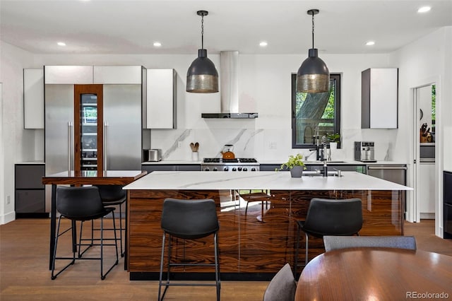 kitchen featuring wall chimney range hood, an island with sink, white cabinets, modern cabinets, and range with gas cooktop
