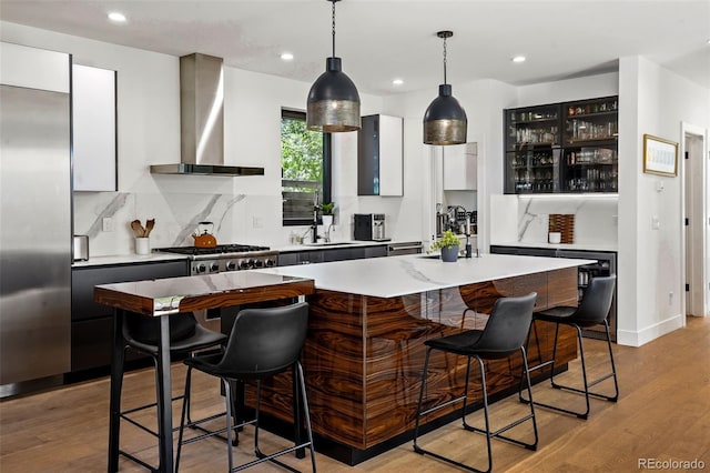 kitchen with tasteful backsplash, light countertops, wall chimney exhaust hood, a kitchen bar, and a sink