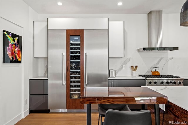 kitchen with white cabinets, wall chimney exhaust hood, light wood-style floors, stainless steel gas stovetop, and beverage cooler