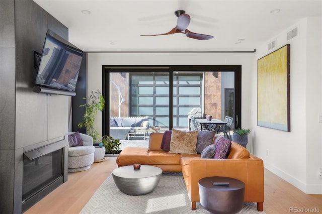 living room with a glass covered fireplace, baseboards, light wood-style floors, visible vents, and ceiling fan