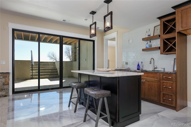 kitchen with sink, hanging light fixtures, a kitchen breakfast bar, light stone counters, and backsplash