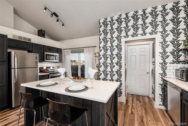 kitchen with lofted ceiling, a breakfast bar area, light hardwood / wood-style flooring, stainless steel appliances, and backsplash