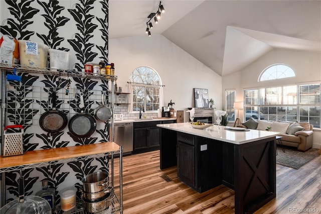 kitchen with high vaulted ceiling, light wood-type flooring, stainless steel dishwasher, a kitchen island, and backsplash