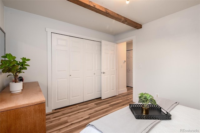 bedroom with beamed ceiling, light wood-type flooring, and a closet