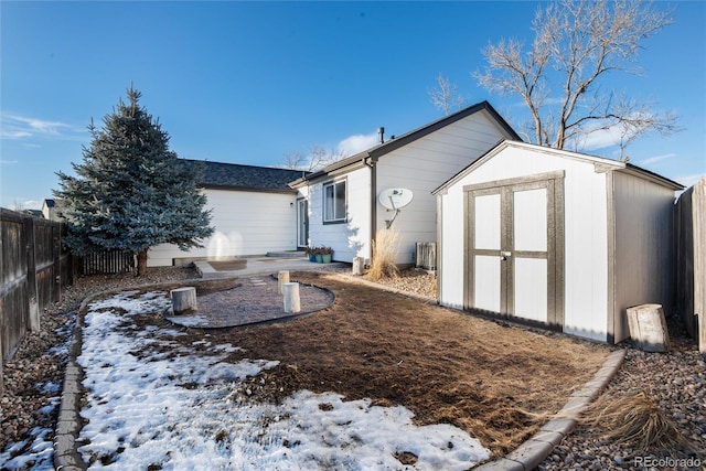 snow covered back of property with an outbuilding, a fenced backyard, and a storage unit