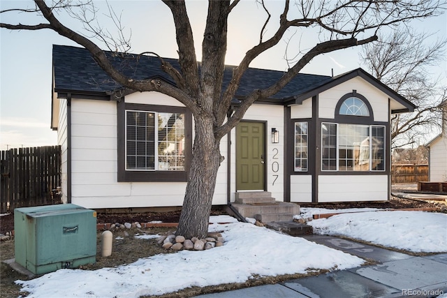 view of front facade with entry steps, a shingled roof, and fence