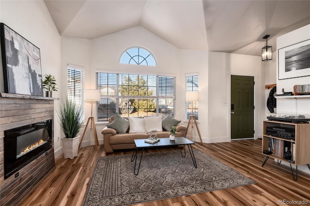 living area with lofted ceiling, wood finished floors, a glass covered fireplace, and baseboards