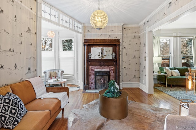 living area featuring a brick fireplace, a notable chandelier, crown molding, and wood finished floors