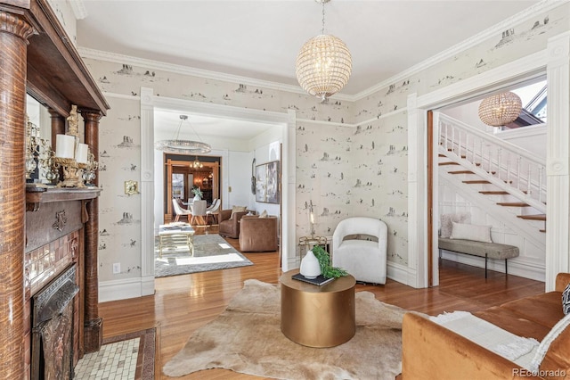 living area with stairs, crown molding, wood finished floors, a chandelier, and wallpapered walls