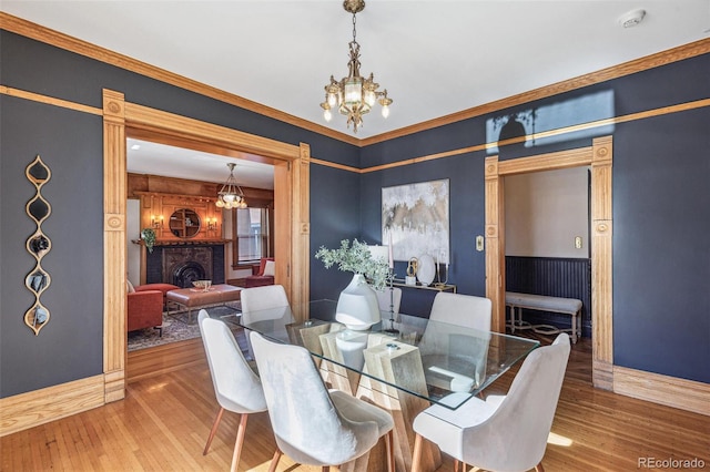 dining area with baseboards, a fireplace, an inviting chandelier, and wood finished floors