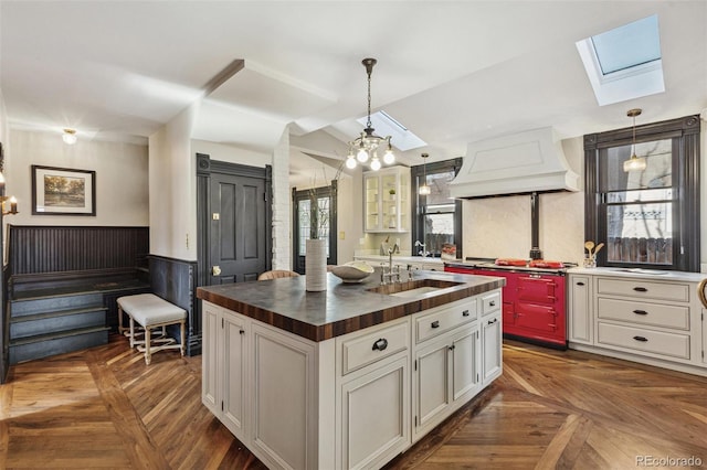 kitchen featuring a skylight, custom exhaust hood, wooden counters, wainscoting, and a sink