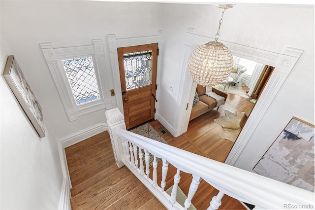 foyer entrance with visible vents, a notable chandelier, baseboards, and wood finished floors