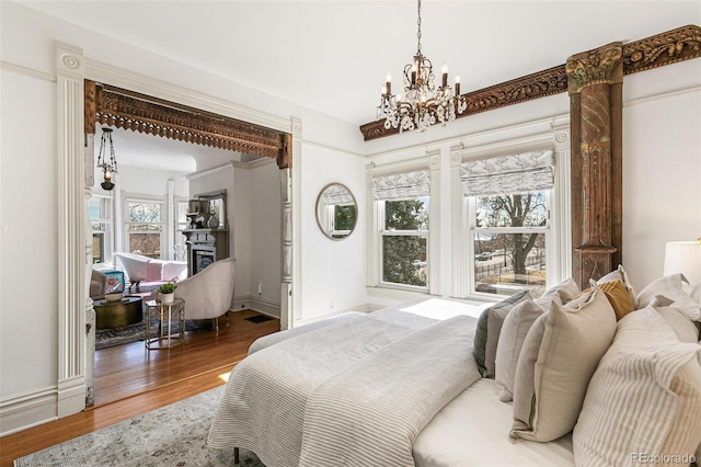 bedroom with a chandelier, a fireplace, wood finished floors, and baseboards