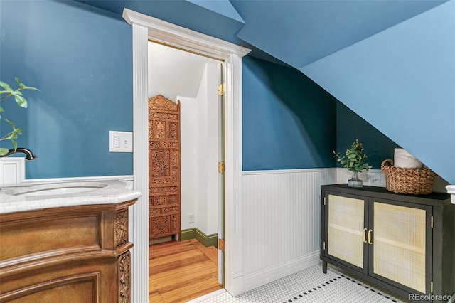 bathroom featuring lofted ceiling, wood finished floors, a sink, and wainscoting