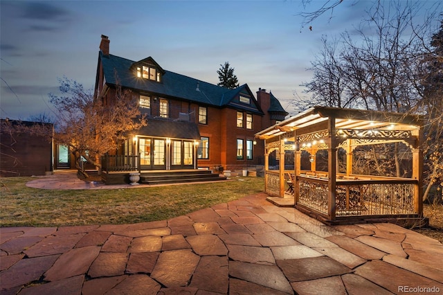 back of house at dusk featuring french doors, a yard, a patio, a chimney, and a pergola