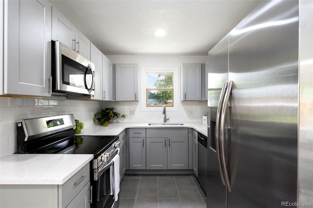 1180 Newark St, Aurora, CO 80010 - kitchen featuring appliances with stainless steel finishes, a sink, gray cabinetry, tasteful backsplash, and dark tile patterned floors