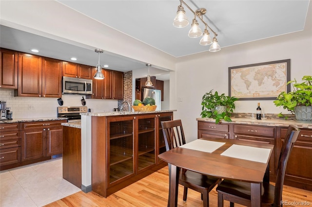 kitchen featuring light stone counters, stainless steel appliances, hanging light fixtures, backsplash, and a sink