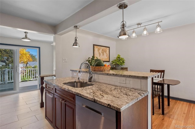 kitchen featuring a kitchen island with sink, a sink, hanging light fixtures, light stone countertops, and dishwasher