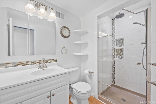 bathroom featuring toilet, vanity, visible vents, a shower stall, and tasteful backsplash