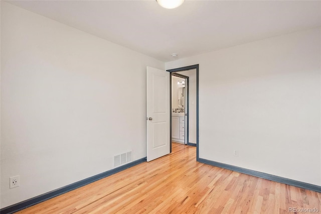 empty room featuring wood finished floors, visible vents, and baseboards